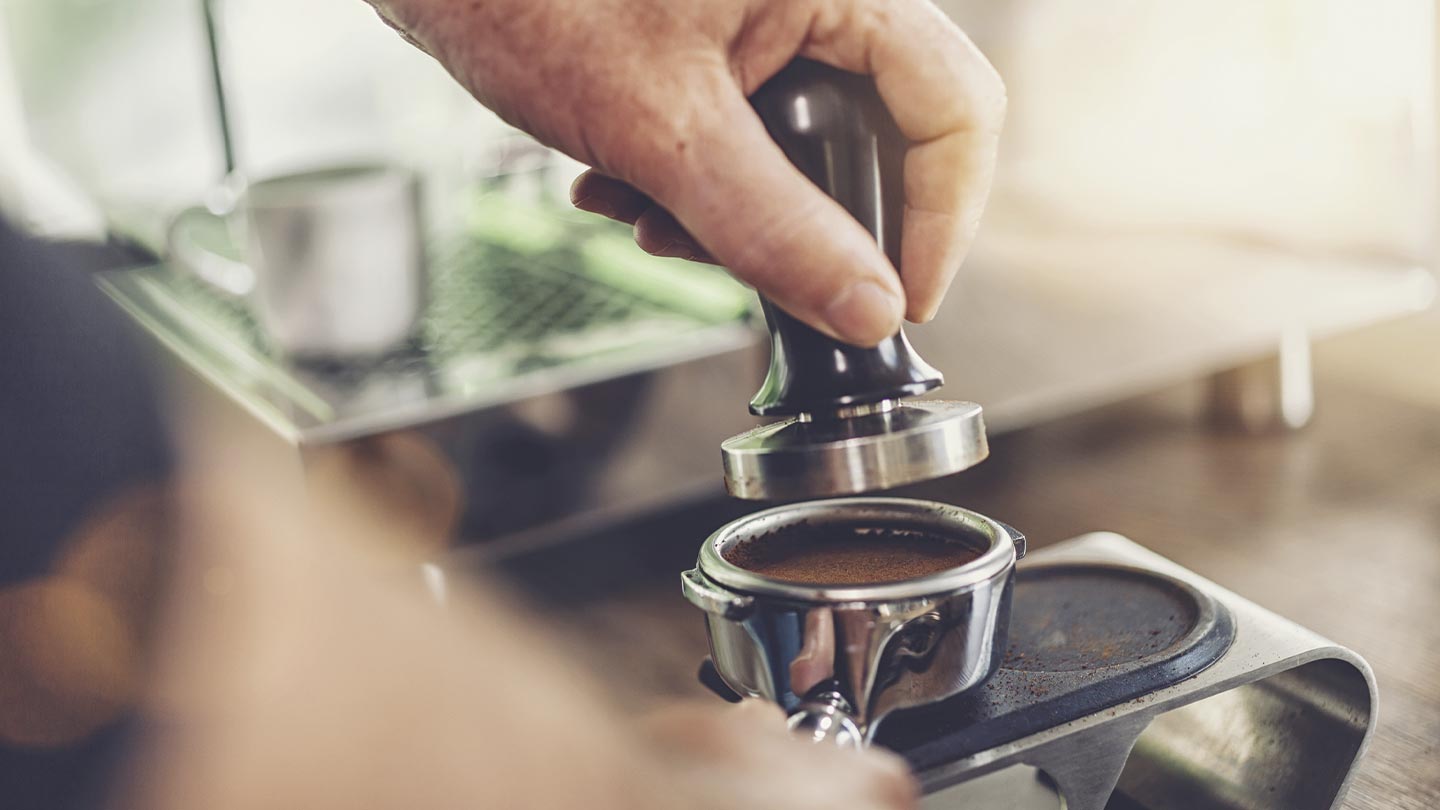 Mano de un barista utiliza herramientas como un tamper y un apisonador para café