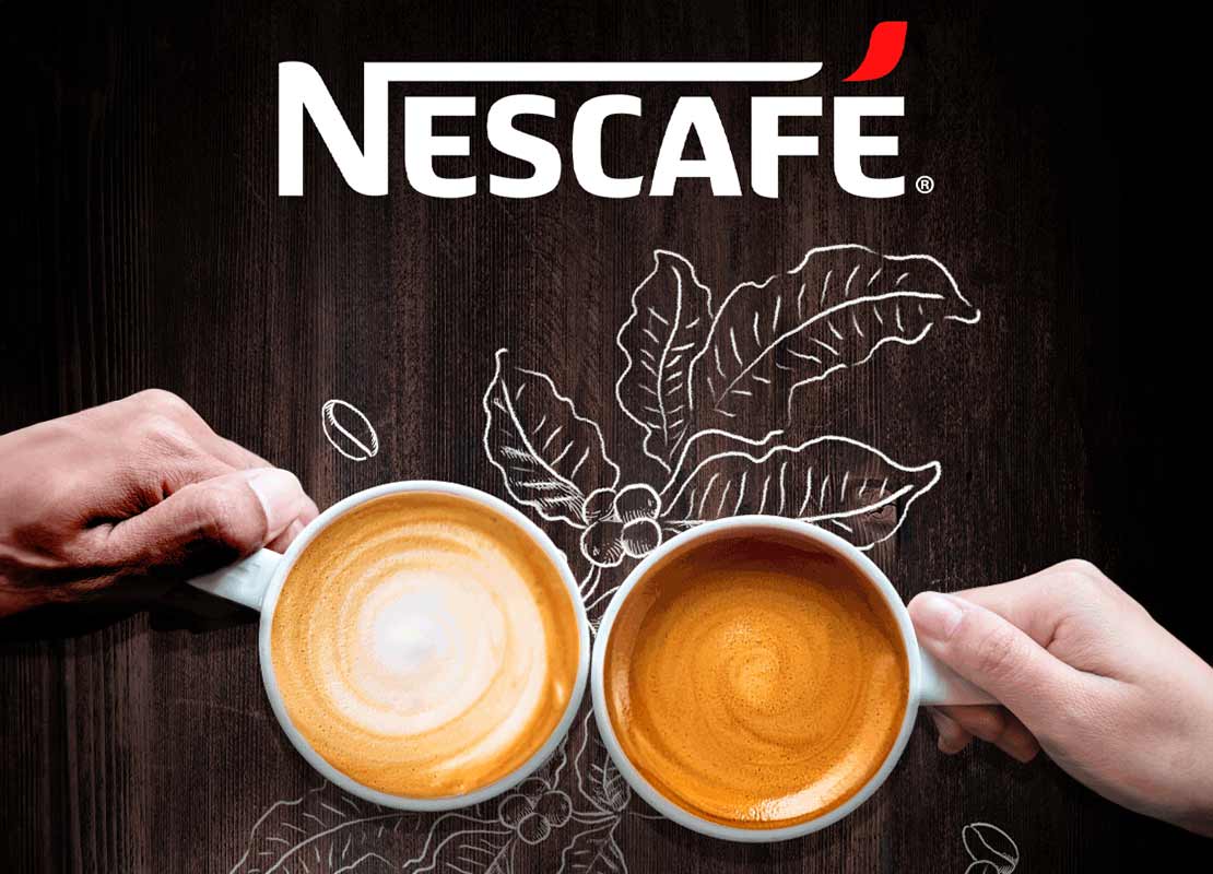 Manos sostienen dos tazas de café colocadas en una mesa de madera con el logo de NESCAFÉ®