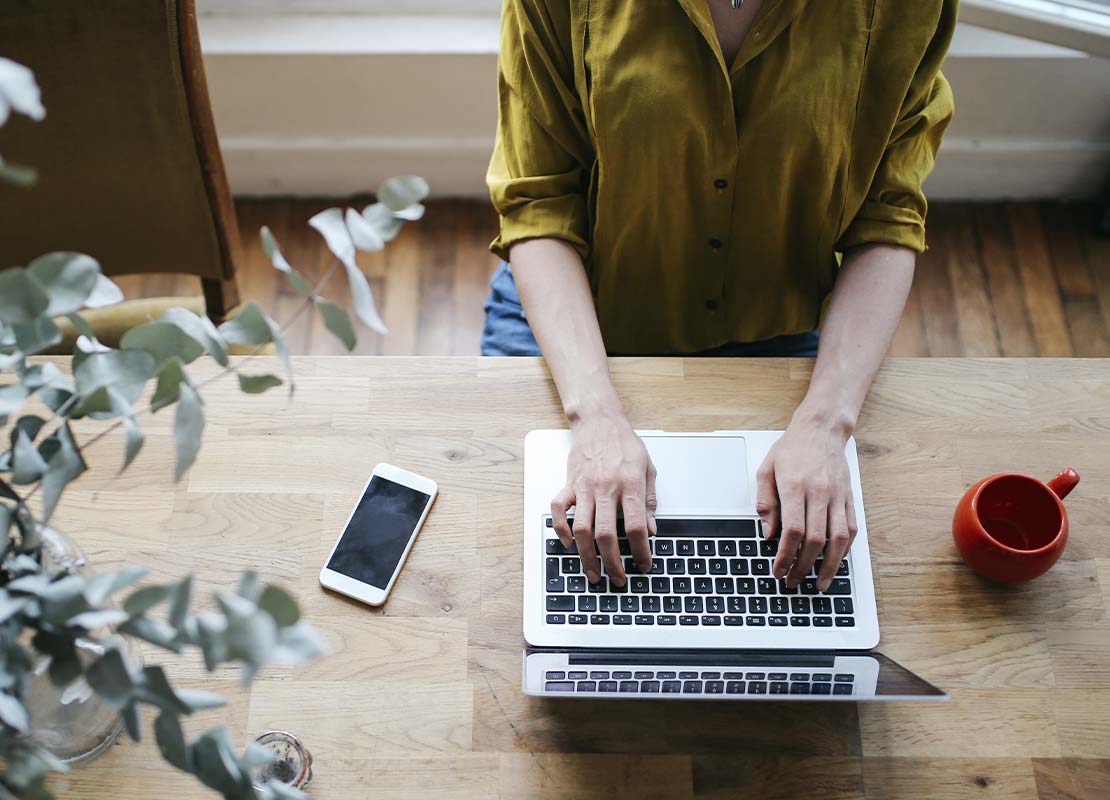 Una mujer sentada a la mesa diseñando el menú de postres para su negocio en una computadora