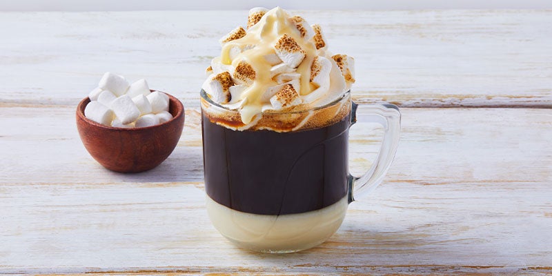 Taza blanca de café bombón decorado con crema batida, leche condensada y masmelos