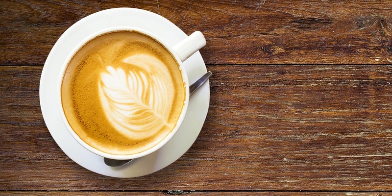 Taza blanca de cappuccino con latte art sobre un plato de cerámica