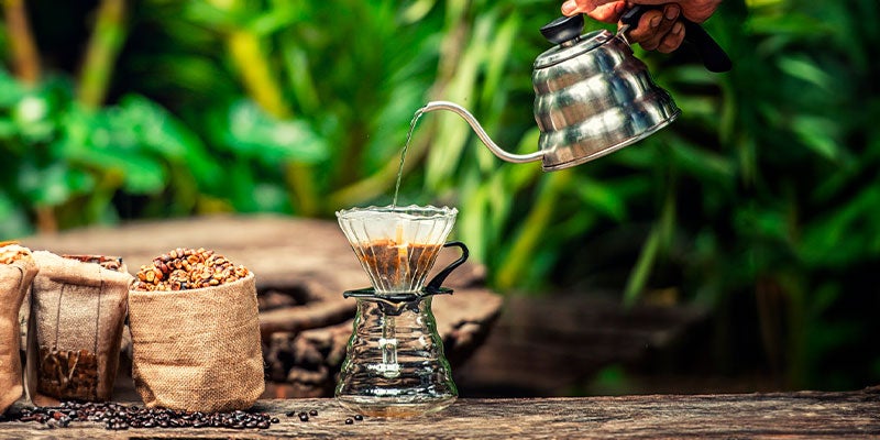Mano sostiene una tetera con la que vierte agua al filtro de café de un dripper