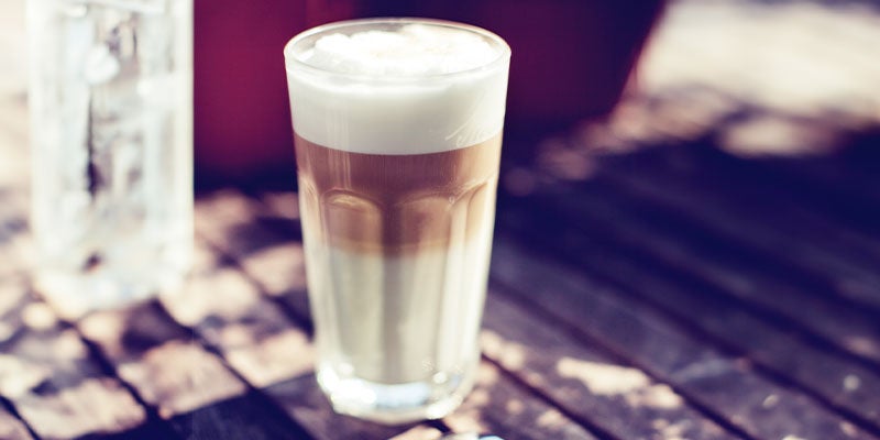 Café macchiato servido en un vaso de cristal alto sobre una mesa de madera