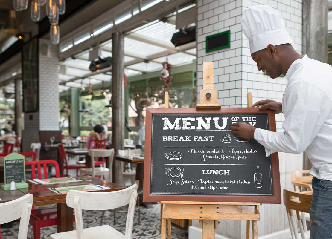 Chef escribe el menú de desayuno en el tablero de la entrada de un restaurante