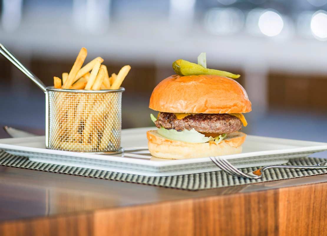 Plato con hamburguesa y cesta de papas fritas en bastones sobre una mesa de madera