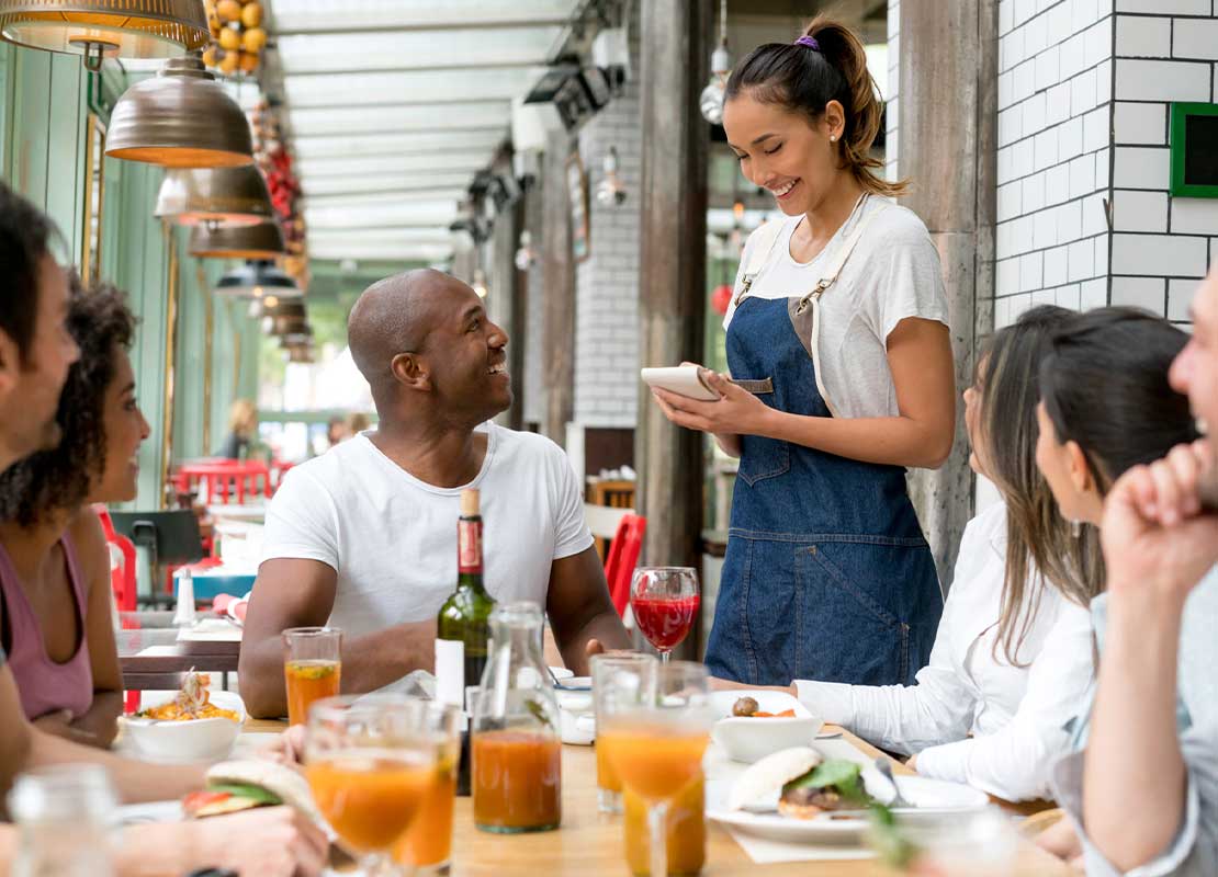 Mesera atiende a un grupo de personas sentados a la mesa en un emprendimiento gastronómico