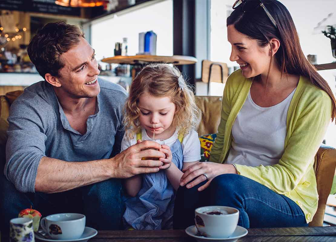 Papá, mamá e hija sonriendo mientras disfrutan de la bebida de un menú infantil en un negocio