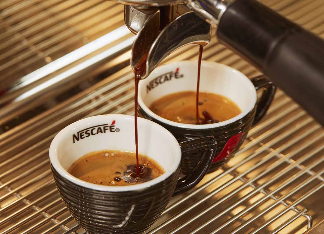Filtro de una máquina vierte café sobre dos tazas negras de cerámica de NESCAFÉ®