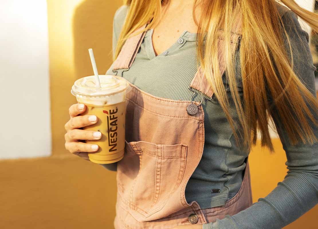 Mujer sostiene en su mano un vaso de NESCAFÉ® con una bebida de café frío