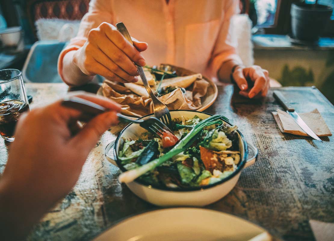 Manos de mujer y de hombre sostienen tenedores mientras comparten un desayuno vegetariano en un restaurante