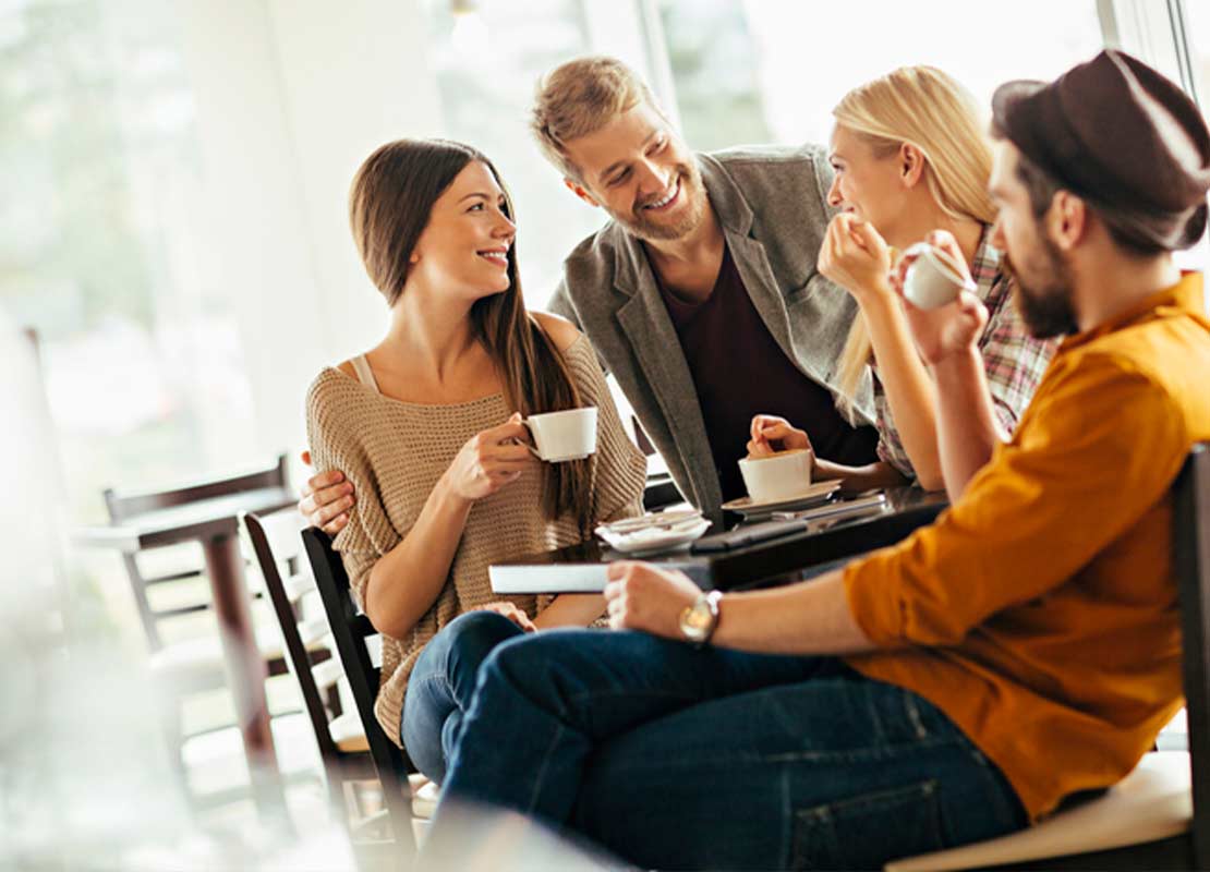 Cuatro amigos sentados en una cafetería conversan mientras beben una taza de café