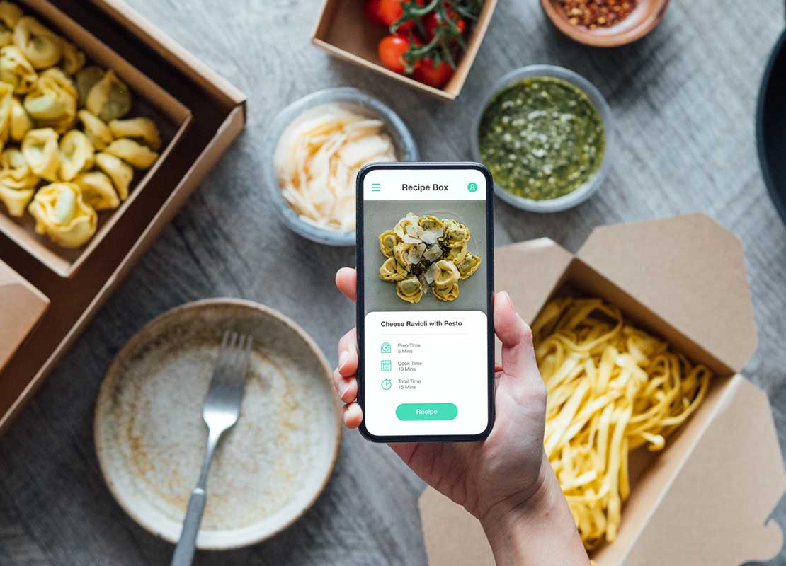 Mano sostiene un celular en el que verifica los platillos en la mesa, pedidos en una app de delivery