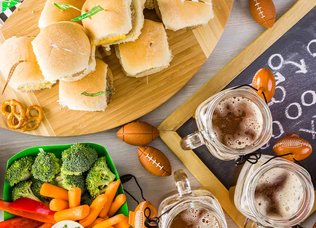 Snacks para cafetería salados: sándwiches, vegetales, salsas y decoración sobre fútbol americano