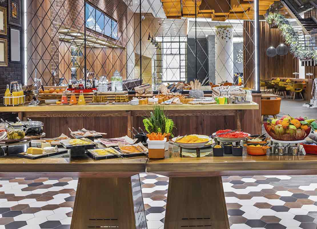 Desayuno tipo buffet con mesas de vegetales, proteínas, frutas, bebidas, entre otras preparaciones