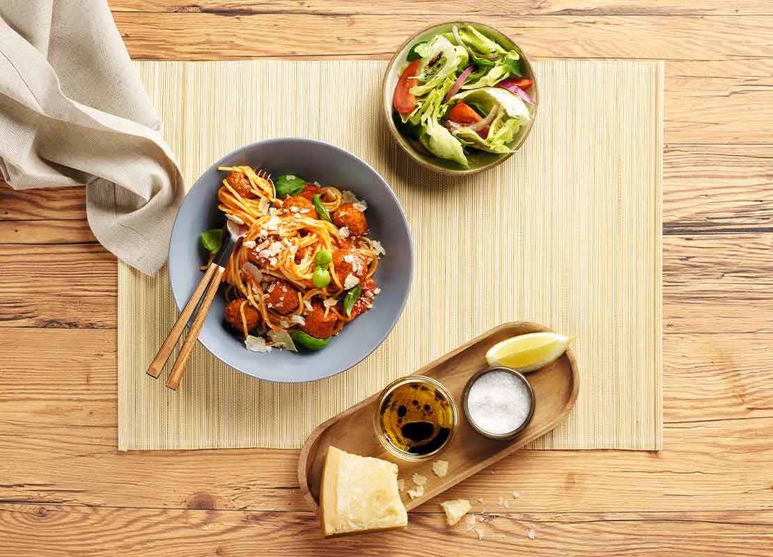 Bowl de fideos y albóndigas veganas, recipientes con ensalada, sal, limón y salsa arbiatta