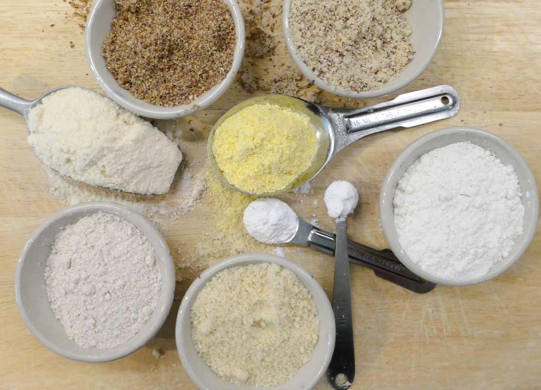 Recipientes con harina de almendra, semilla de lino, maíz, trigo integral y más insumos para repostería