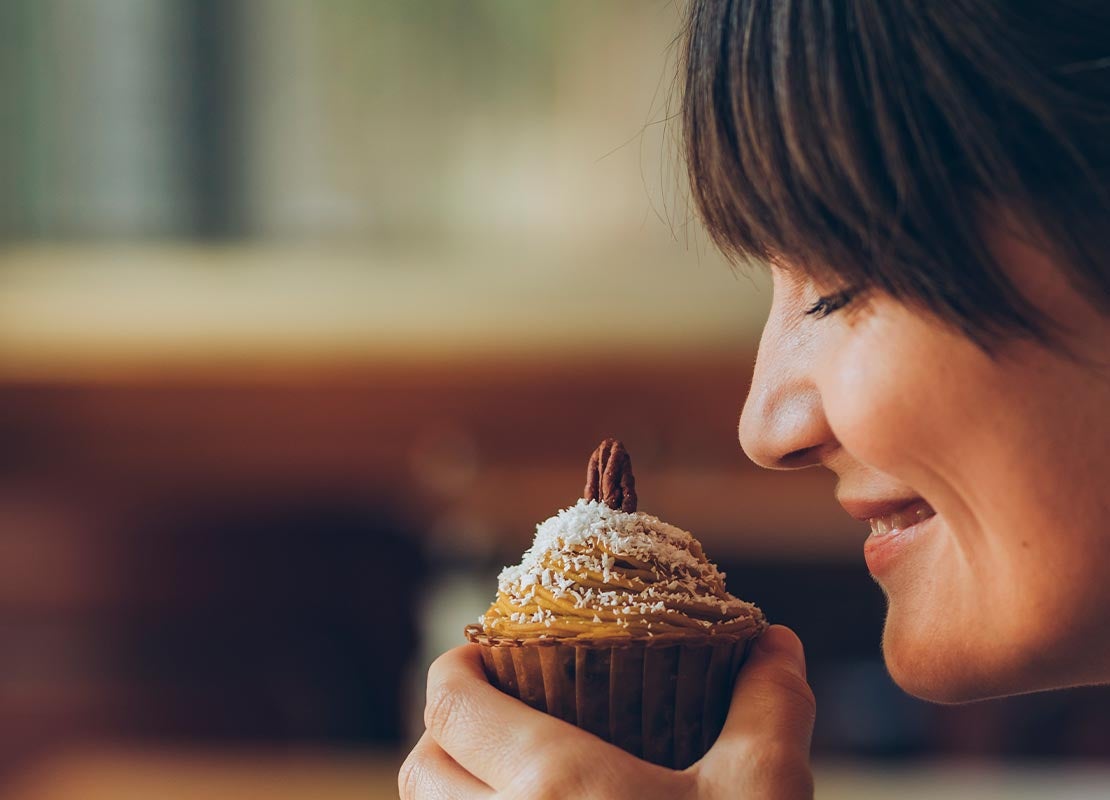 Con los ojos cerrados, mujer disfruta del aroma de un cupcake que sostiene frente a su rostro