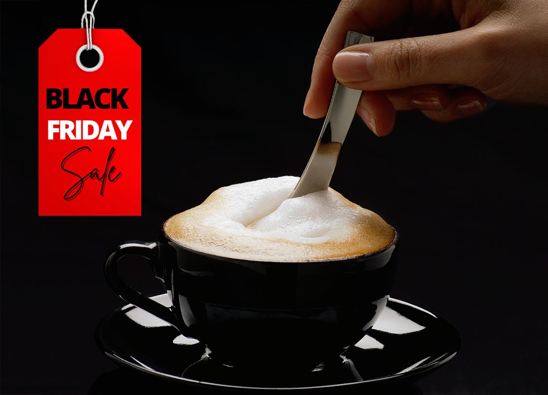 Mano mezcla un cappuccino en taza negra, al lado una etiqueta de “Black Friday Sale”