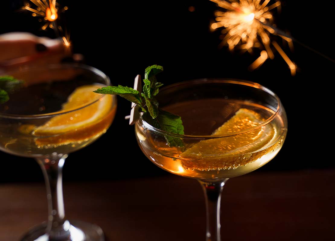 Dos copas con cócteles sin alcohol con rodajas de naranjas, al fondo fuegos artificiales