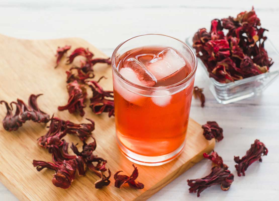 Vaso de mocktail de jamaica con hielo sobre una tabla rodeada de este ingrediente