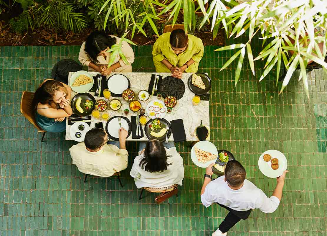 5 personas sentadas a la mesa de un restaurante decorado con plantas esperan comida que lleva un mesero