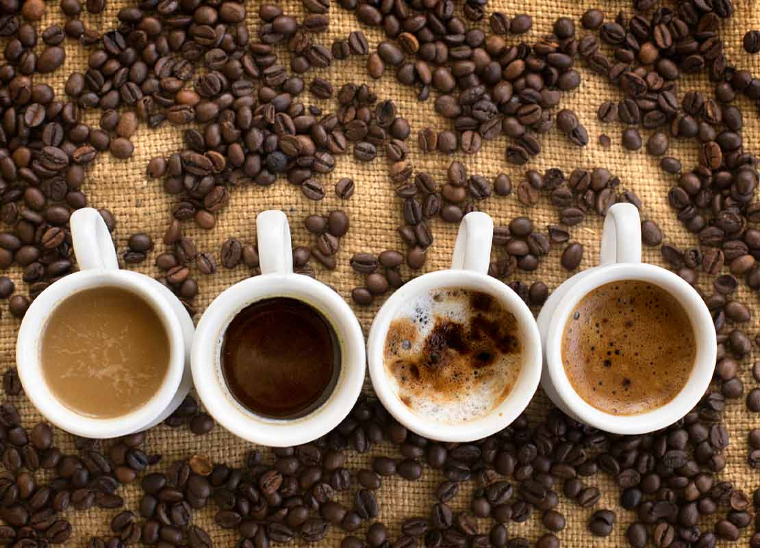 4 tazas con diferentes bebidas calientes rodeadas de granos de café tostado NESCAFÉ®