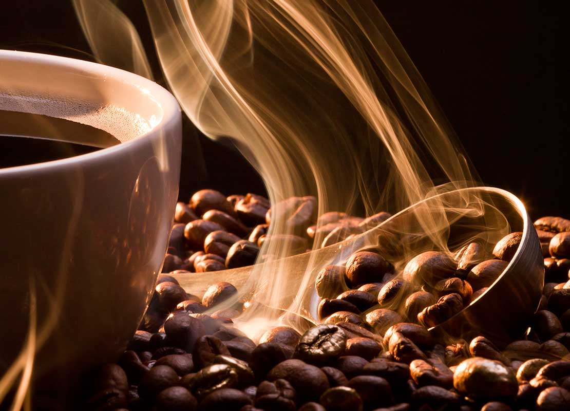 Taza de café humeante rodeada por granos de café NESCAFÉ® y una cuchara medidora metálica