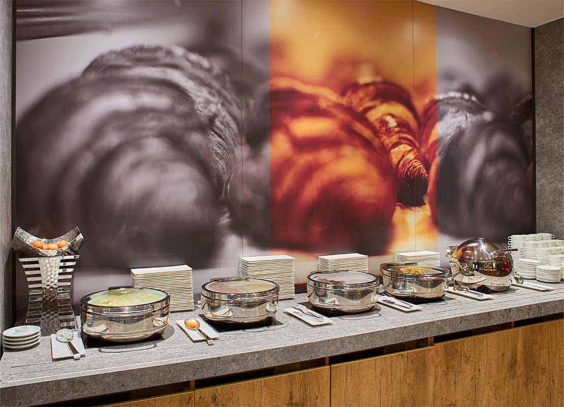 Buffet de hotel con diferentes recipientes de comida variada, cubiertos, platos, eentre otros insumos