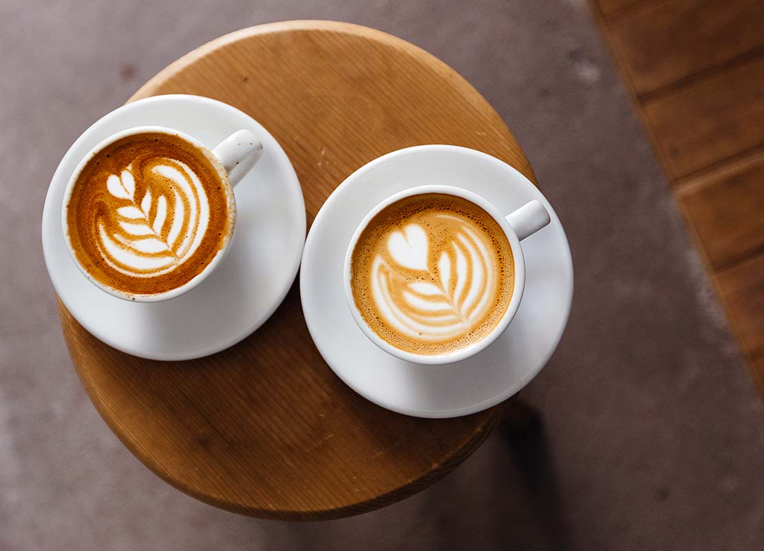 Dos tazas de cappuccinos NESCAFÉ® con latte art sobre una mesa pequeña de madera