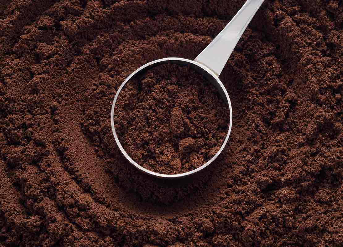 Café tostado y molido dentro de una cuchara de acero inoxidable y alrededor de esta