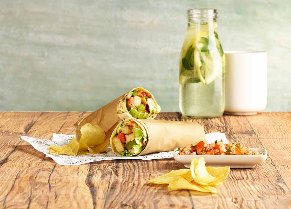 Burrito de vegetales y granos, al lado papas fritas, pico de gallo y botella de agua saborizada