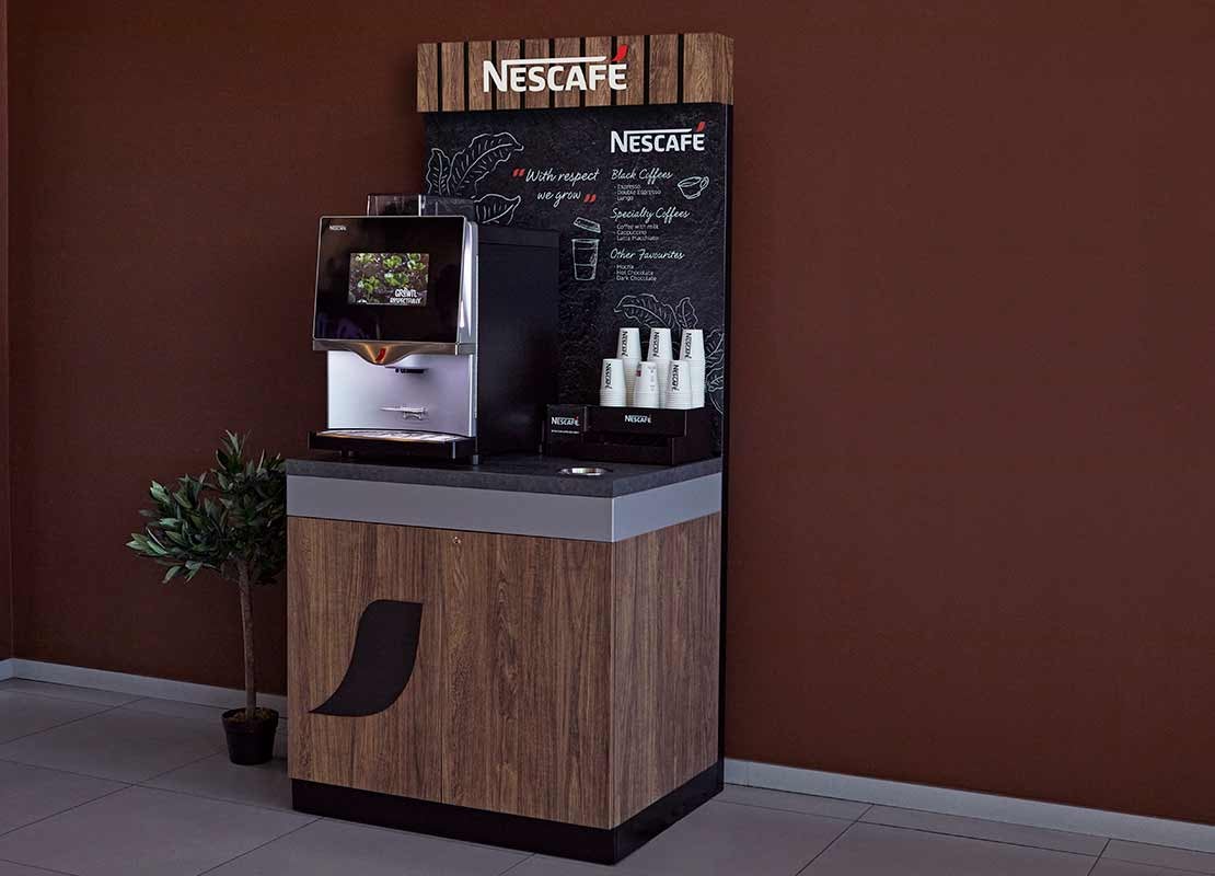 Mueble de madera sostiene una máquina NESCAFÉ®, vasos, tapas y material POP
