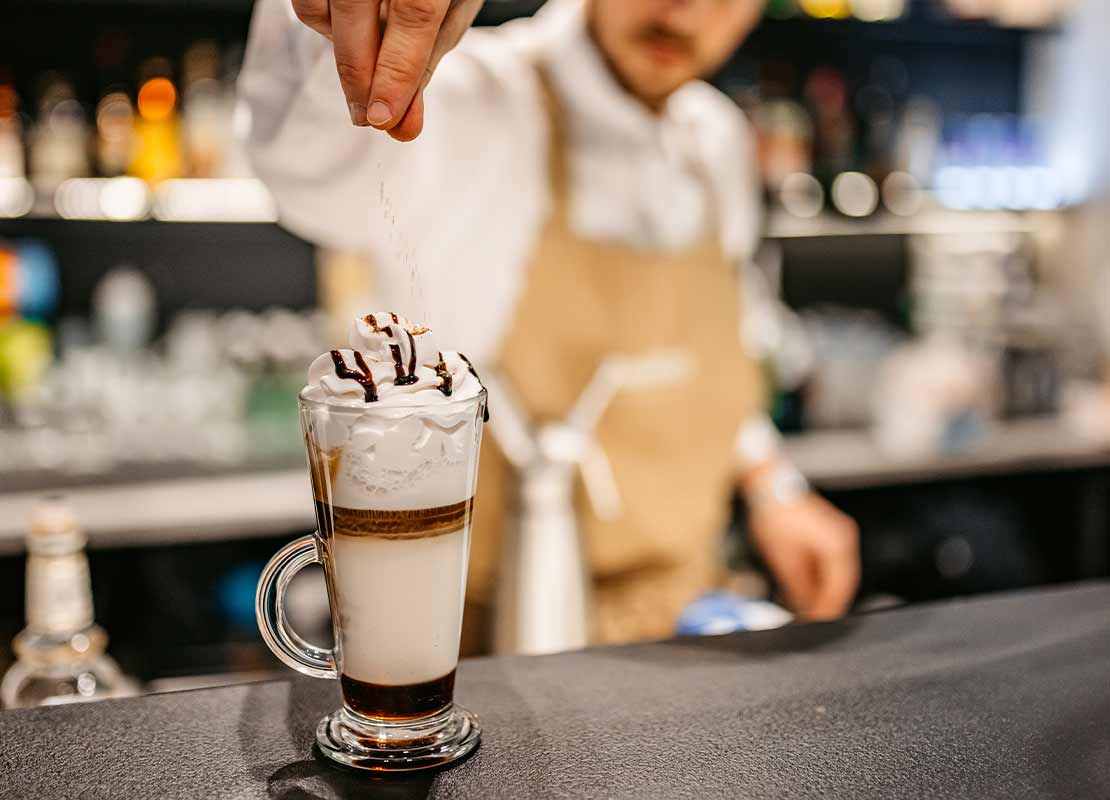 Barman finaliza una bebida de café decorada con crema Chantilly servida en una copa
