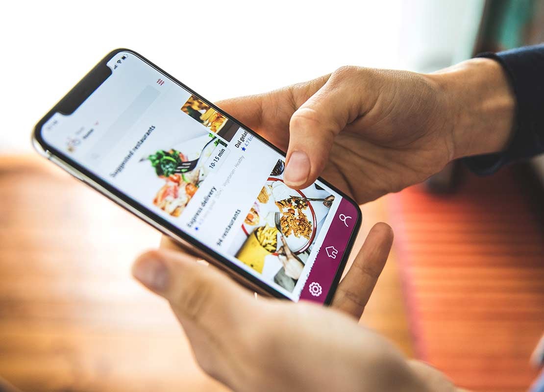 Persona sostiene un celular en el que revisa platillos en la app de domicilios de un restaurante