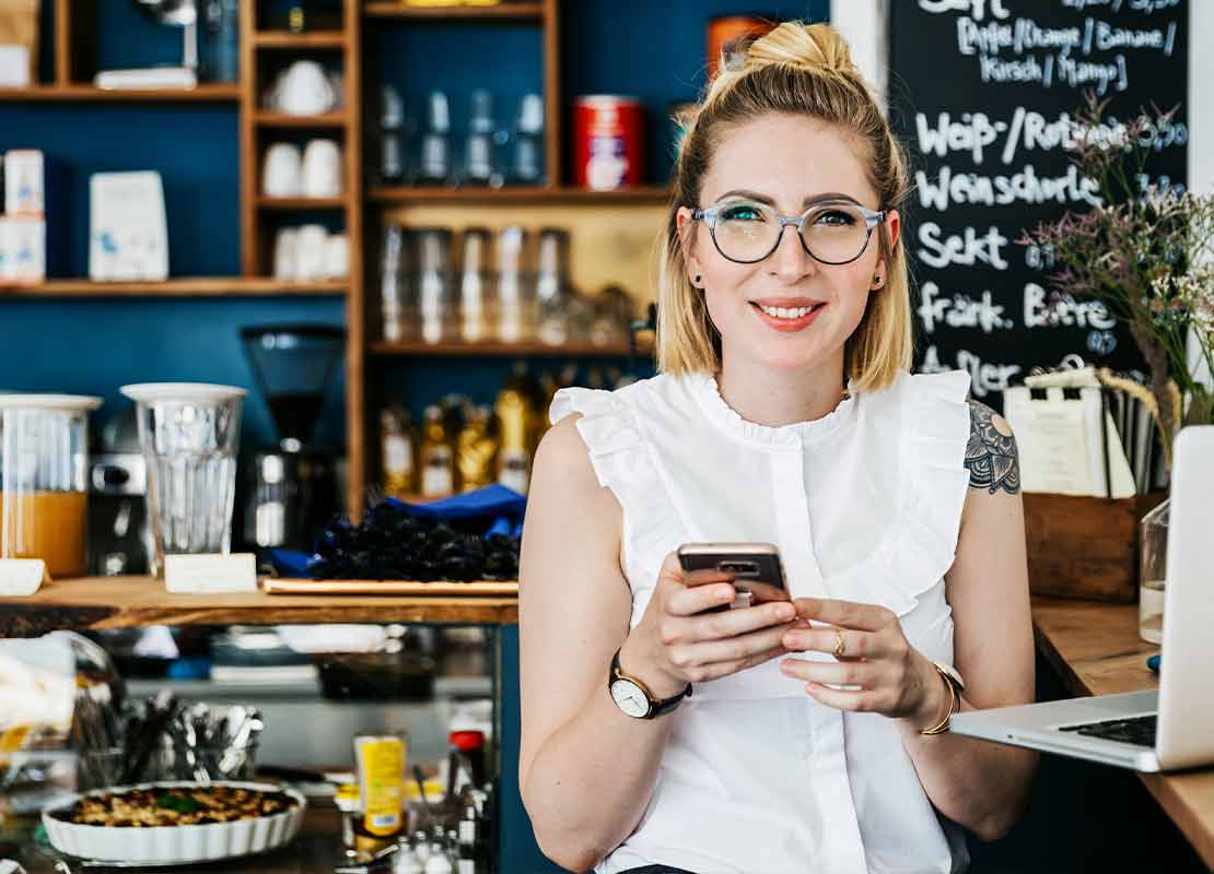 Dueña de un restaurante con un celular y un computador revisa su sistema POS en la nube