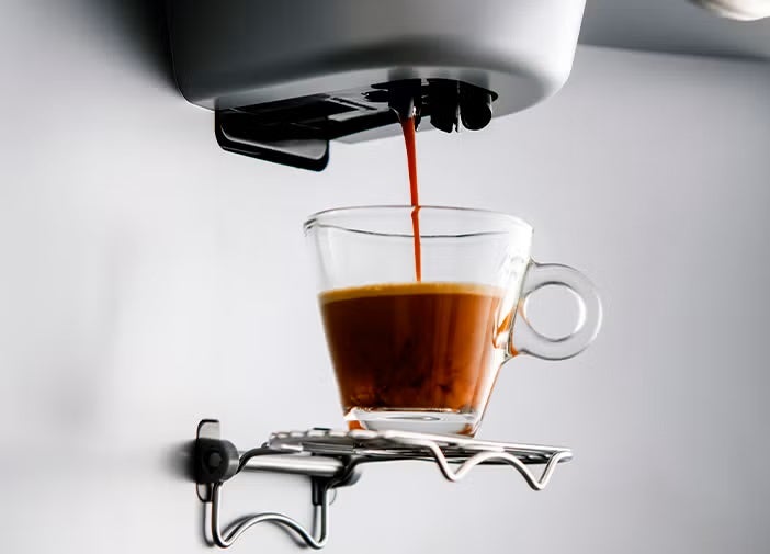 Máquina de café preparando espresso en una taza de vidrio transparente.