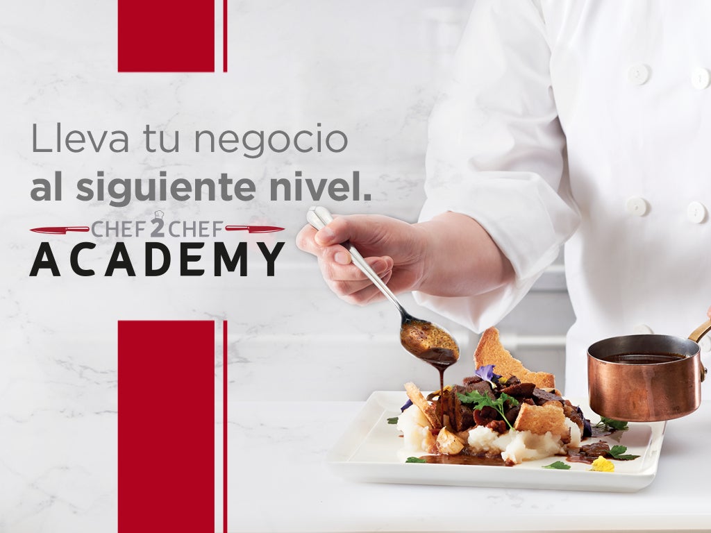 Una persona con bata blanca de Chef 2 Chef Academy, prepara un plato con ingredientes frescos y técnicas profesionales