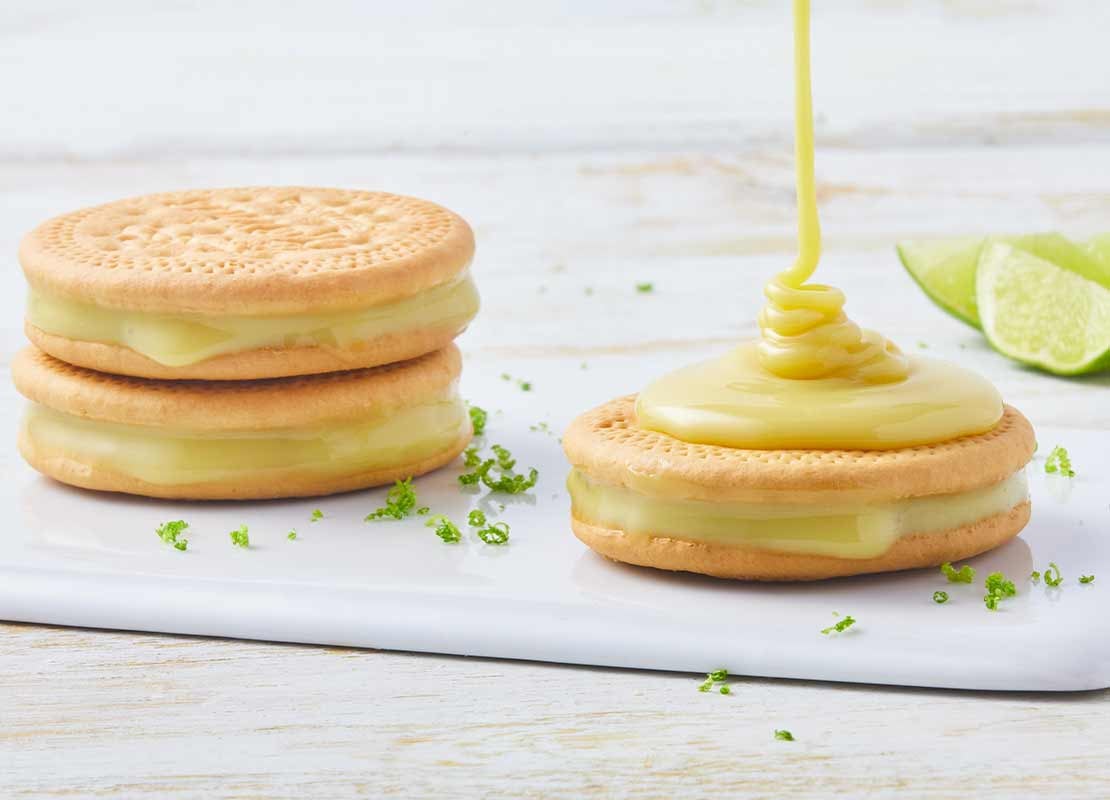 Sobre una tabla de cortar, galletas rellenas de crema de limón y sobre una cae leche condensada