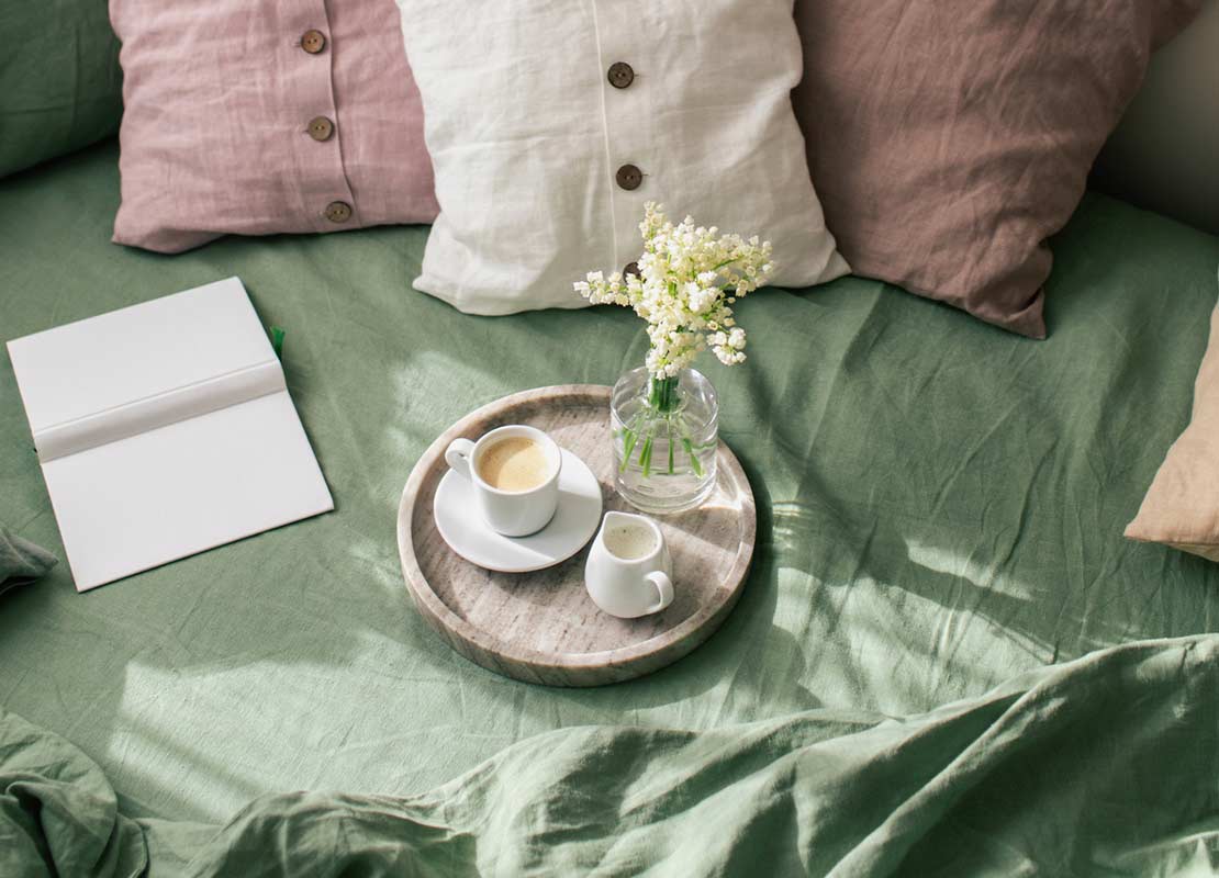 Cama de la habitación de un hotel con almohadas de colores y un servicio de café y leche sobre una bandeja