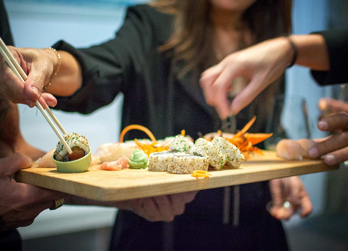 Mujer toma un maki con palillos de una tabla con sushi que un camarero sostiene en sus manos