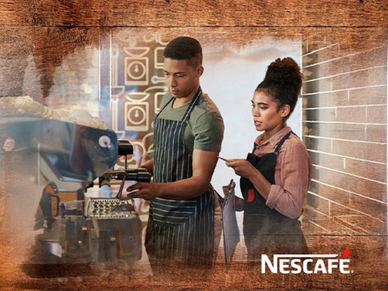 Un barista y un experto NESCAFÉ® con delantales preparando café en una cafetera profesional NESCAFÉ®.