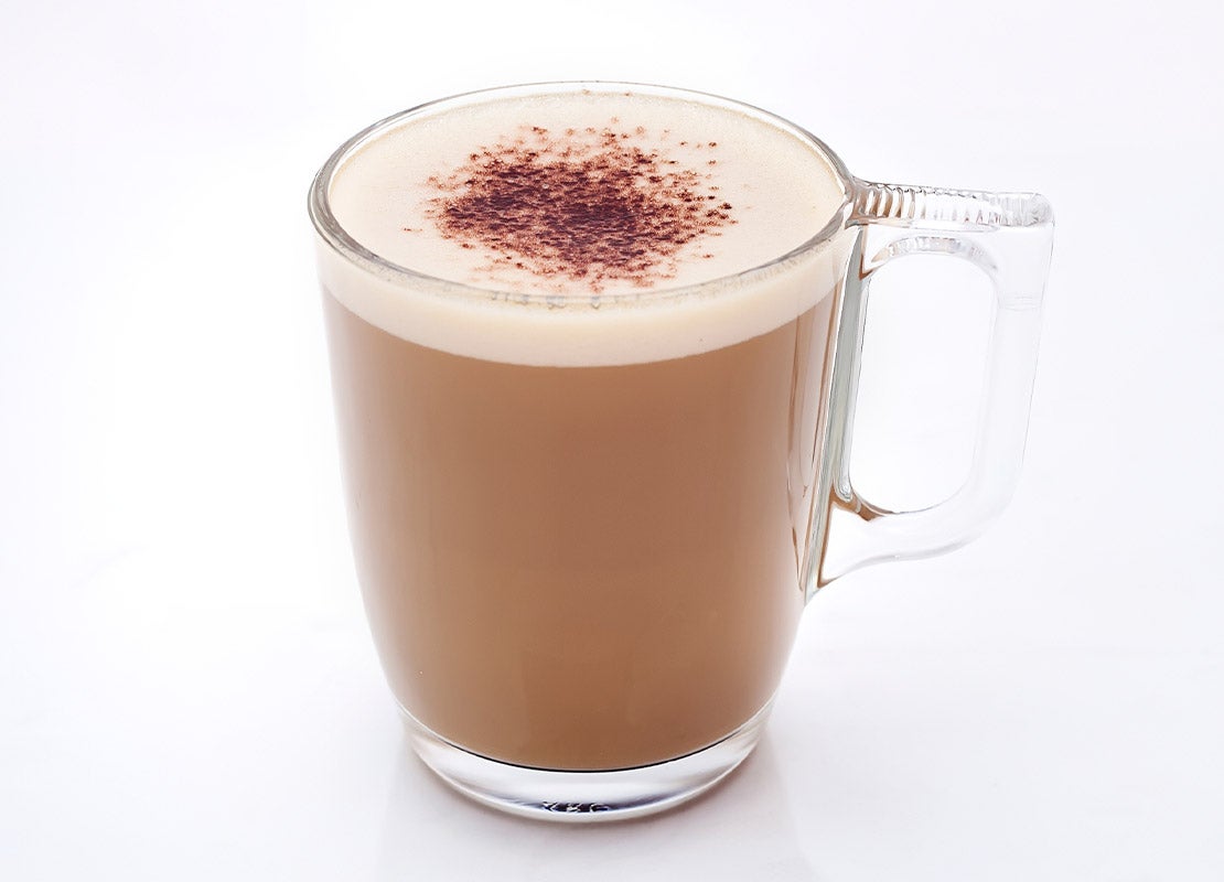 Taza de cristal con cappuccino NESCAFÉ® decorada con canela en la superficie