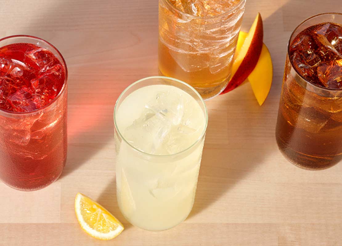 4 vasos de cristal con flavored sparkling water, al lado, cortes de fruta como limón, naranja y mango