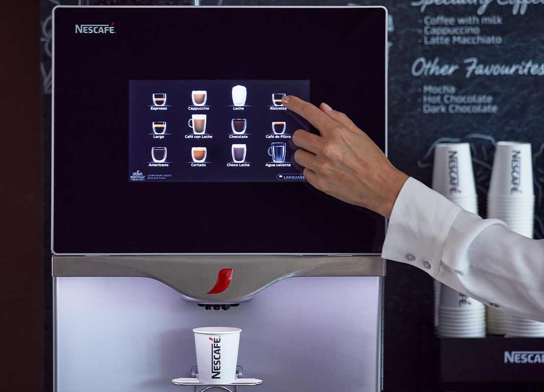 Mano toca el tablero digital de una máquina NESCAFÉ® para elaborar una bebida de café