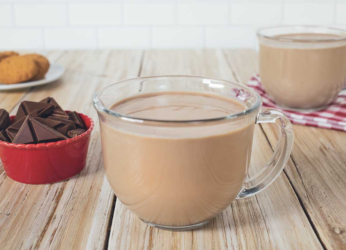 Dos tazas de cristal con chocolate caliente sobre una tabla, al lado, tabletas de chocolate y galletas