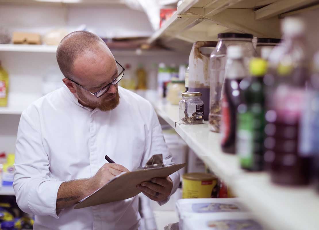 Dos chefs revisan una tablet, sentados a la mesa de una oficina sobre la que hay vasos