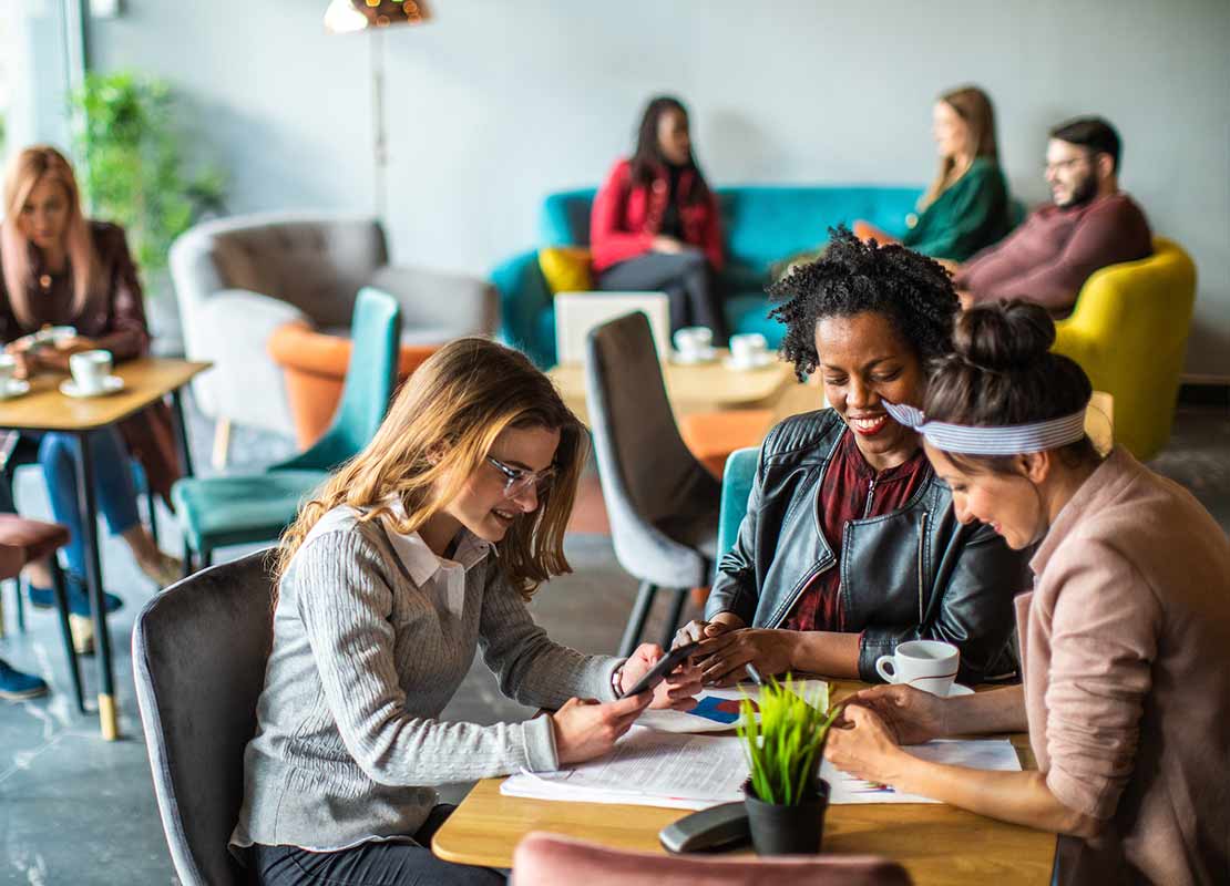 Clientes de una cafetería sentados en diferentes mesas revisan sus celulares mientras beben café