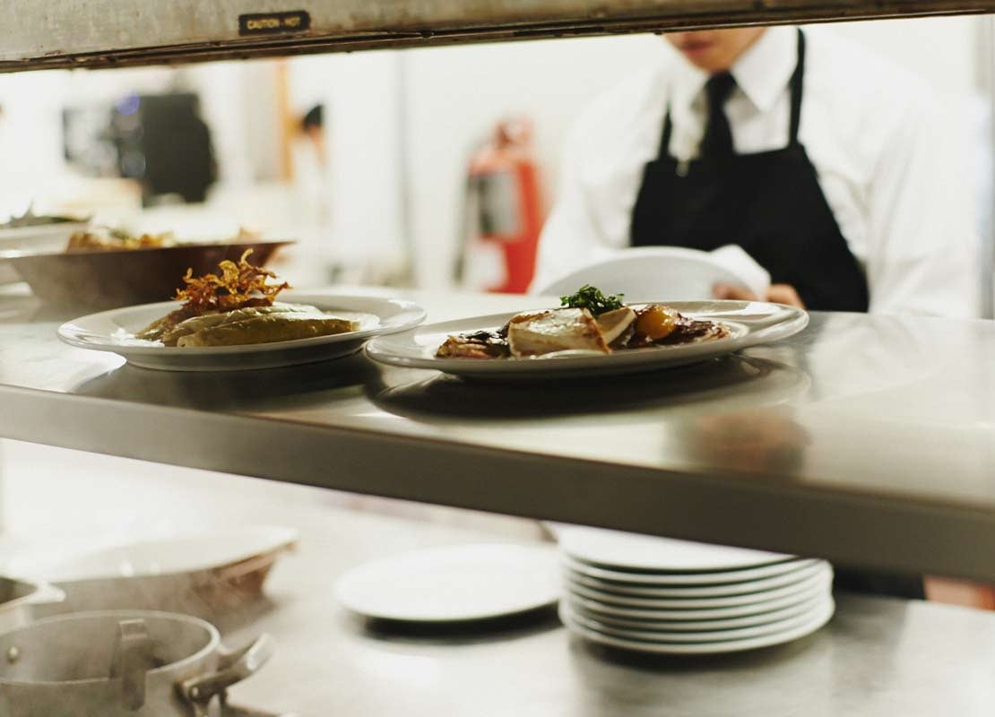 Platos servidos en el mostrador de una cocina, esperando a ser recogidos por el mesero del fondo