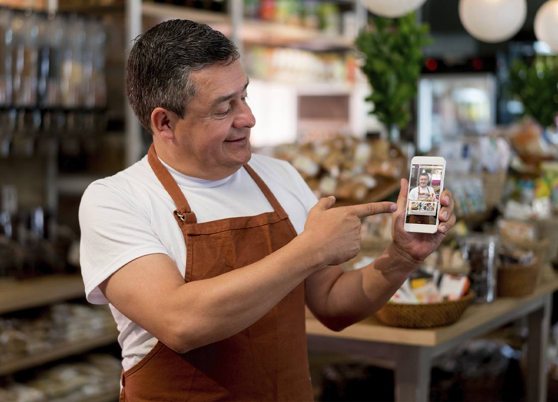 Dueño de una cafetería sostiene un celular y lo señala mostrando sus promociones online