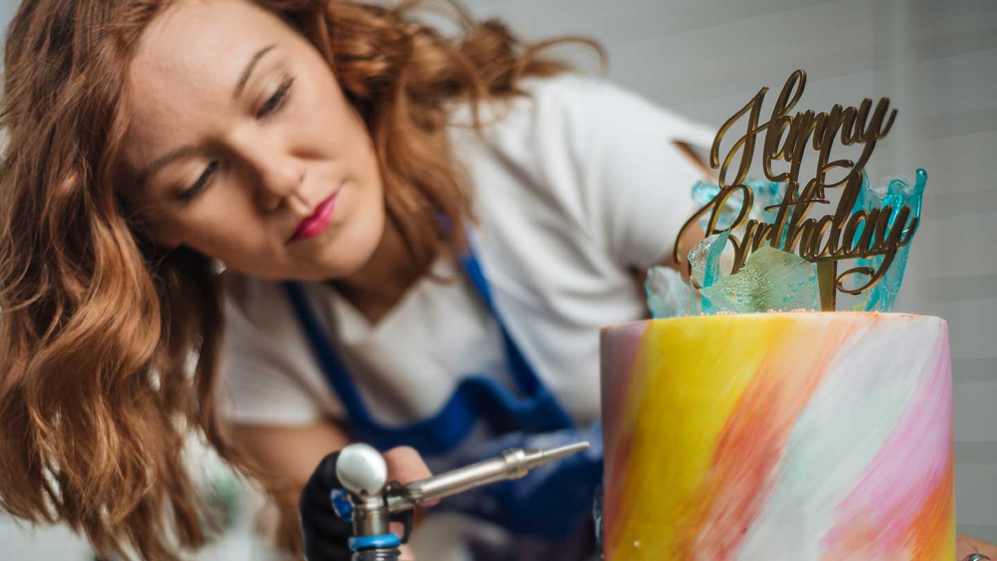 Repostera decora con aerógrafo un pastel con colores degradados y el letrero “happy birthday”